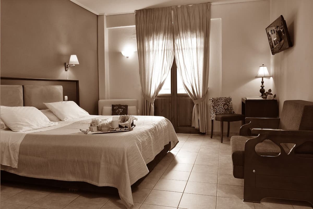 A hotel room with a bed, bedside table, lamp, chair, and a view of the outside through a window.