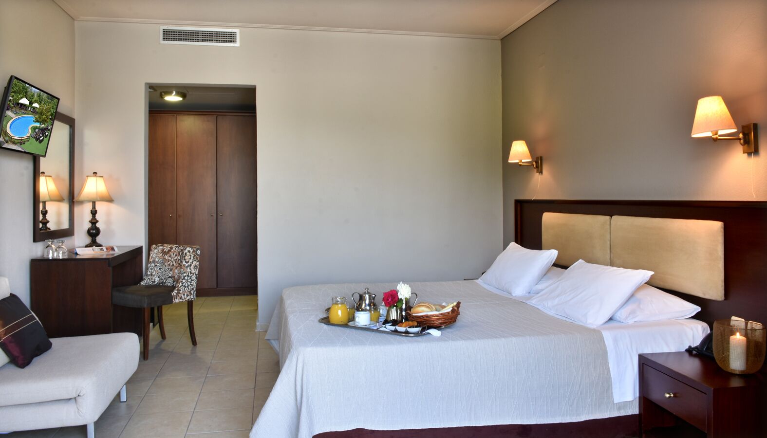 A hotel room with a bed, a desk, a chair, and a breakfast tray on the bed.