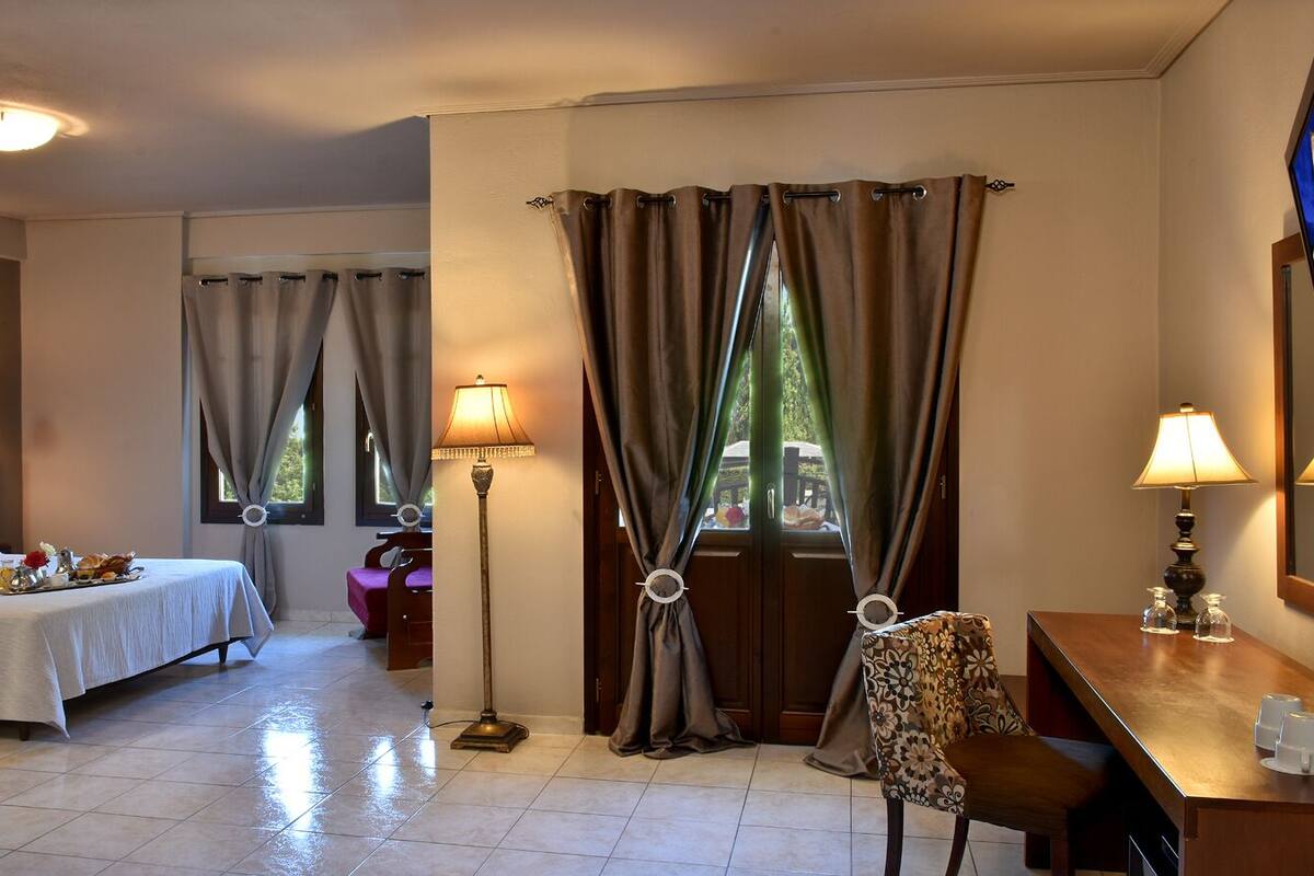 A hotel room with two beds, a desk, a chair, a lamp, and a window with curtains.