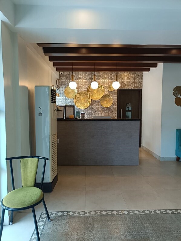 Zona de recepción con diseño moderno, que incluye un mostrador oscuro, papel tapiz estampado y lámparas decorativas colgantes.