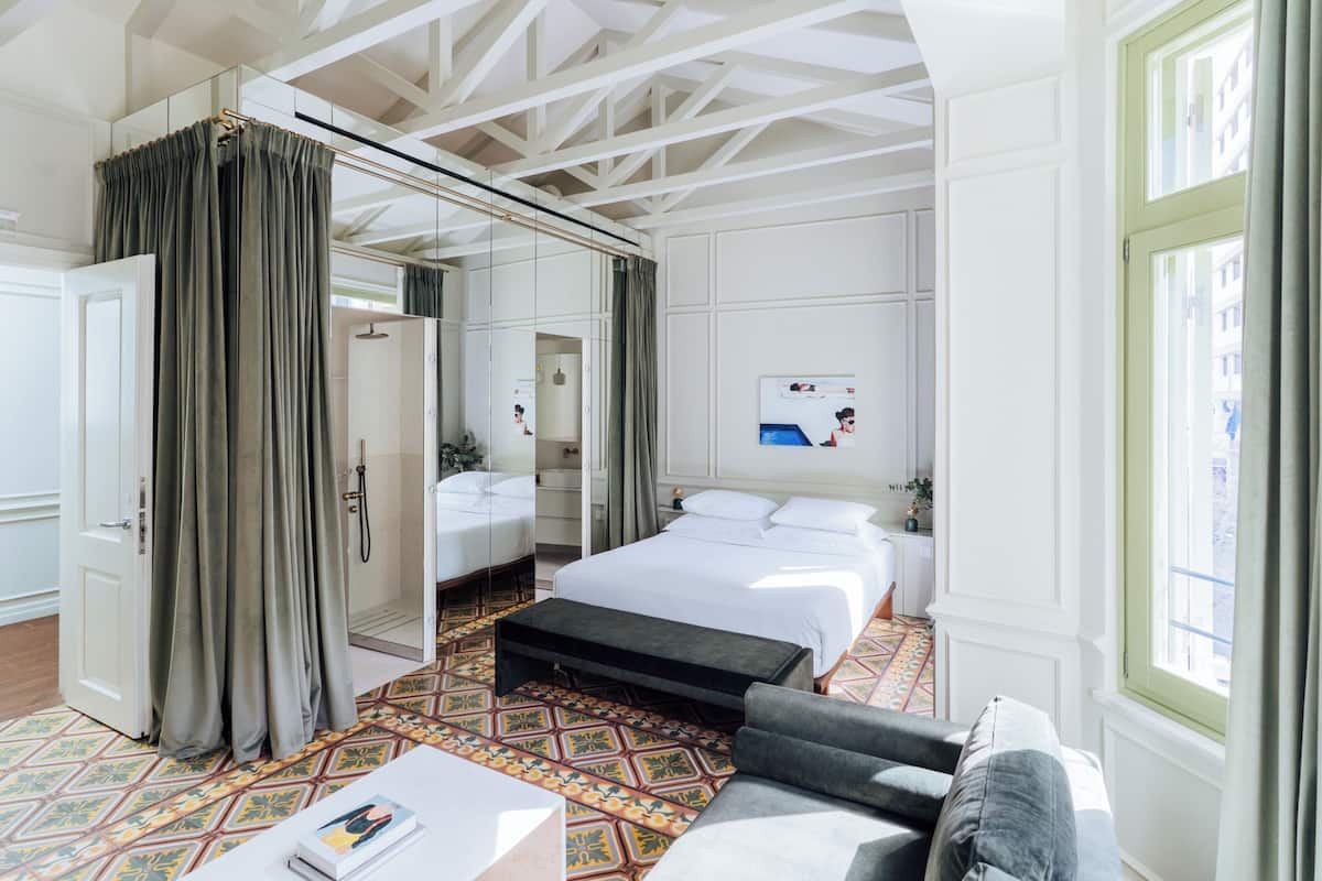 Una habitación de hotel moderna con una cama grande, un sofá, una mesita pequeña y un vestidor.
