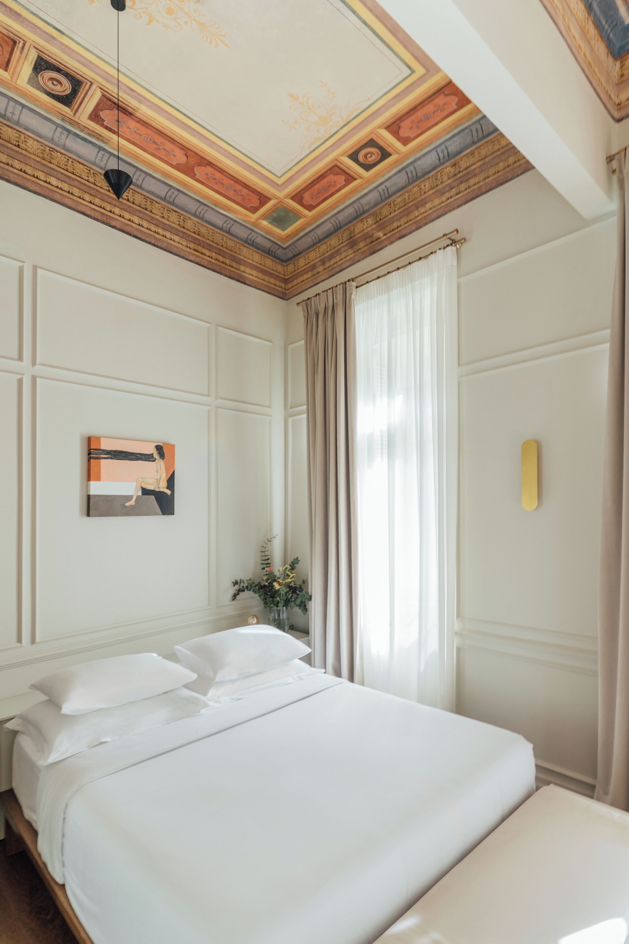 A hotel room with a large bed, a painting on the wall, and a decorative ceiling.
