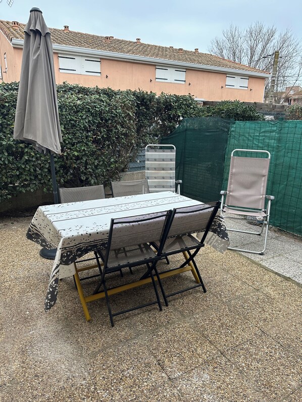 An outdoor patio with a table and chairs, a covered umbrella, and a green fence.