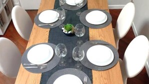 A dining table set with white plates, silverware, and clear wine glasses, centered on a dark placemat.