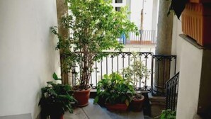 A narrow corridor with potted plants, a white wall, and a balcony with a railing.