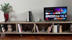 A wooden entertainment unit with a flat-screen TV displaying a streaming service interface, a vase with flowers, and a small plant.