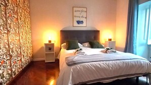 A bedroom with a bed, two bedside tables, a wall with a floral pattern, and a window with curtains.