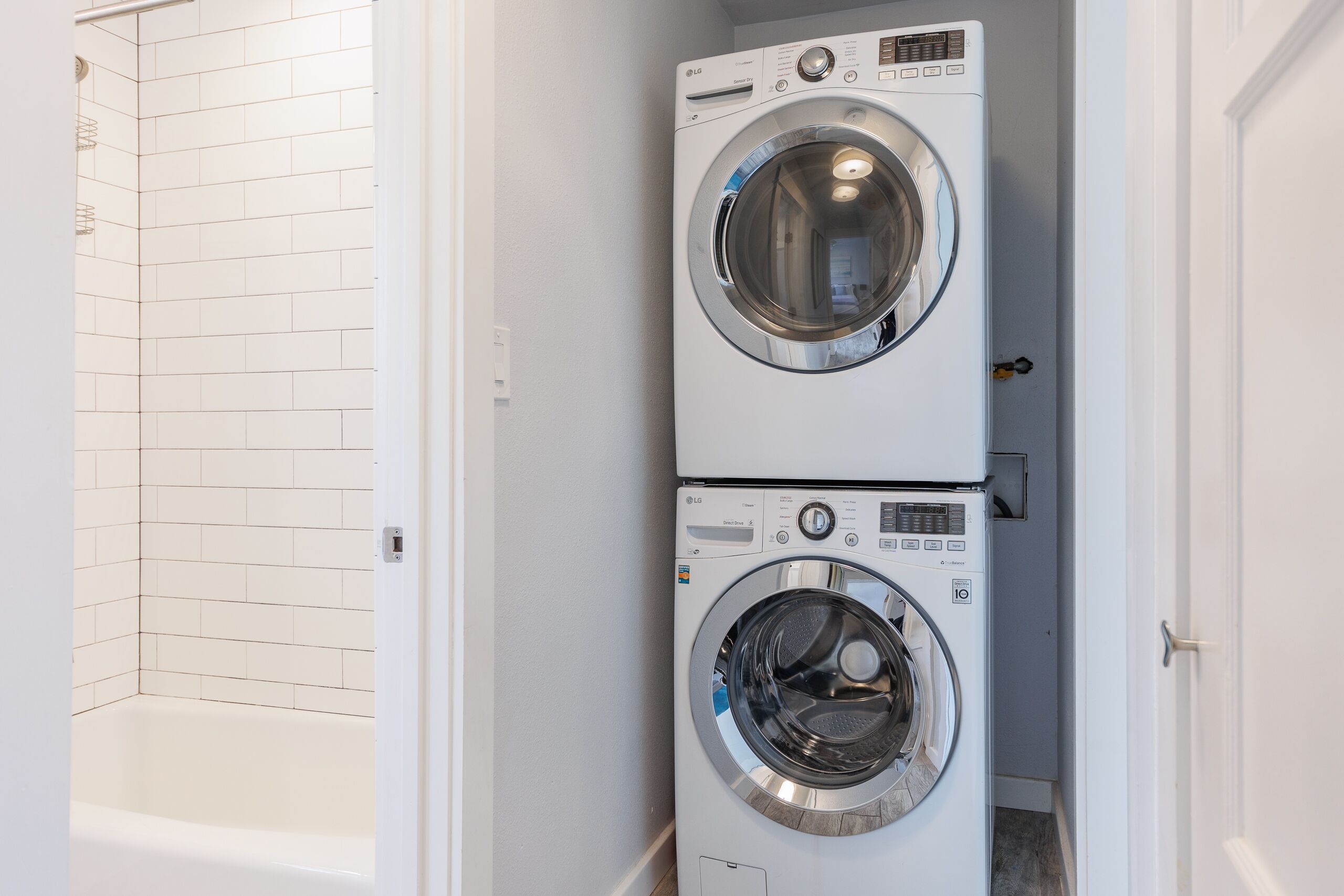 A laundry room with two stacked front-loading washing machines and a white tiled shower area.