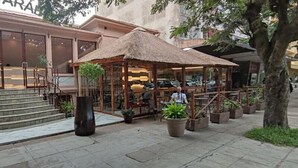 A building with a staircase leading to a glass door, a covered outdoor seating area with tables and chairs, and potted plants. - Villa das Arabias (Maputo)