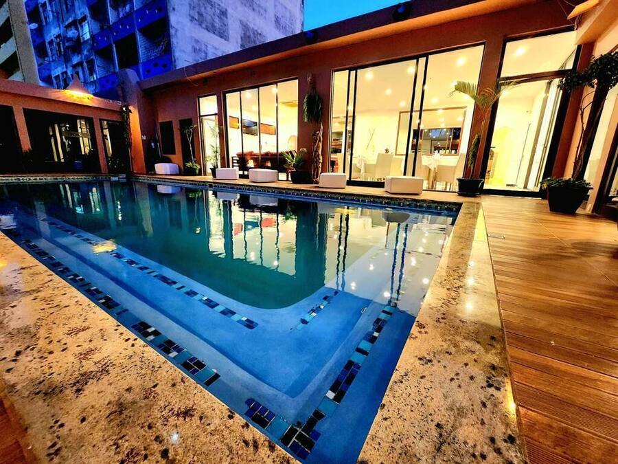 A swimming pool with a tiled deck, adjacent to a building with large windows and indoor seating.