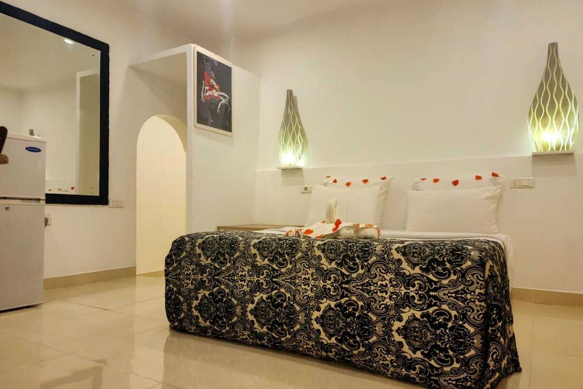 A modern hotel room with a large bed, a mirror, a small table, and a wall-mounted light fixture.