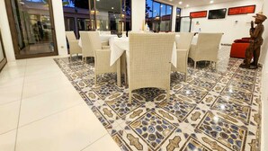A dining area with wicker chairs and a tiled floor, large windows, and a statue. - Villa das Arabias (Maputo)