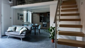Un salon moderne avec un canapé, une table à manger et des chaises. Un escalier mène à l’étage supérieur.