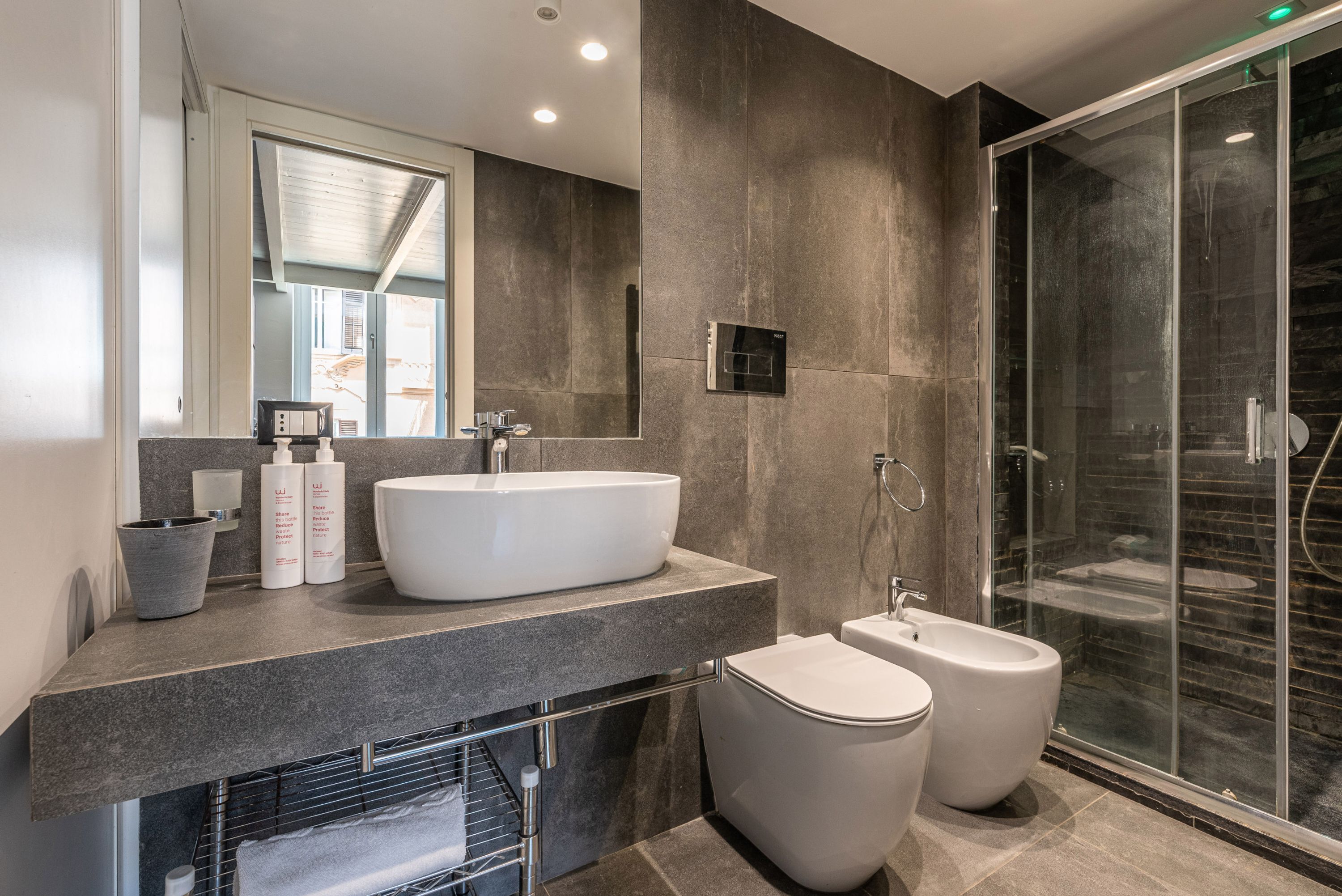 A modern bathroom with a large white sink, a bidet, and a glass-enclosed shower.