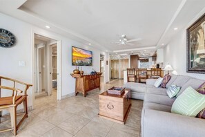 Un salon spacieux avec un canapé, une table basse en bois et un téléviseur. On aperçoit à l’arrière-plan un coin repas avec une table et des chaises.