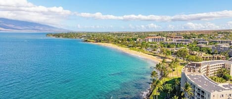 A coastal resort with beachfront properties, a clear blue sea, and a mountainous backdrop.