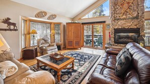A spacious living room with a stone fireplace, leather sofa, and a large window offering a view of the outdoors.