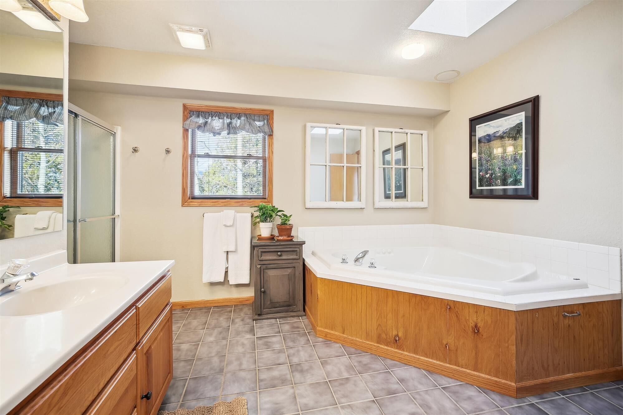 A bathroom with a large bathtub, a double sink vanity, and a window with curtains.