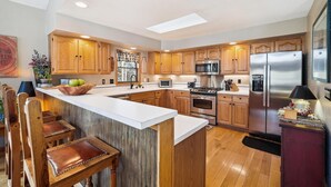 A spacious kitchen with wooden cabinets, a central island with seating, a stainless steel refrigerator, and a microwave.