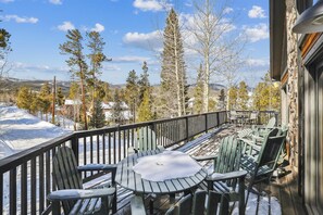 A wooden deck with outdoor seating, overlooking a snowy landscape and trees.