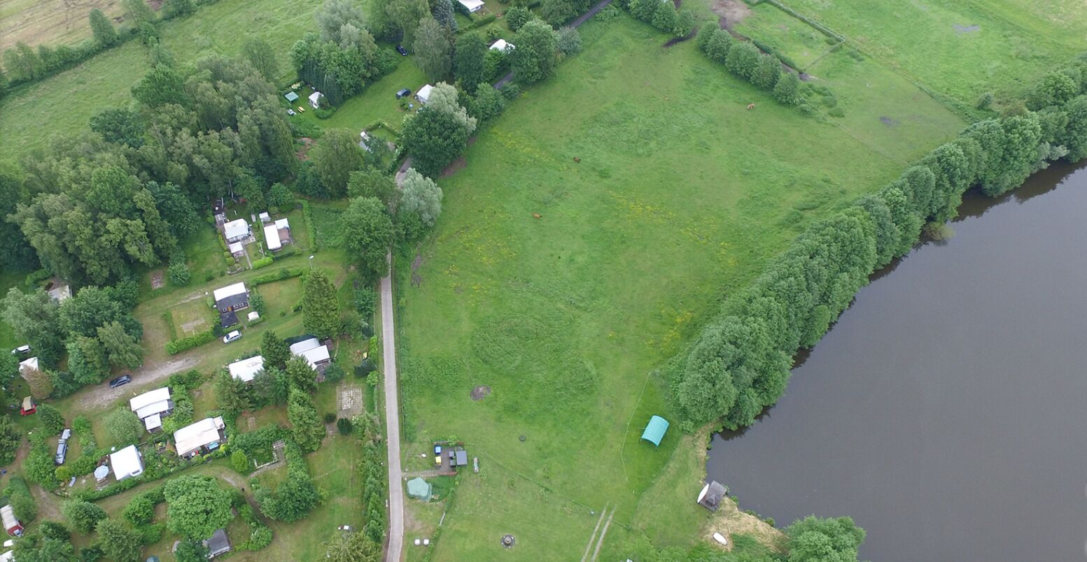 An aerial view of a rural property with several small buildings, a large open grassy area, and a body of water.