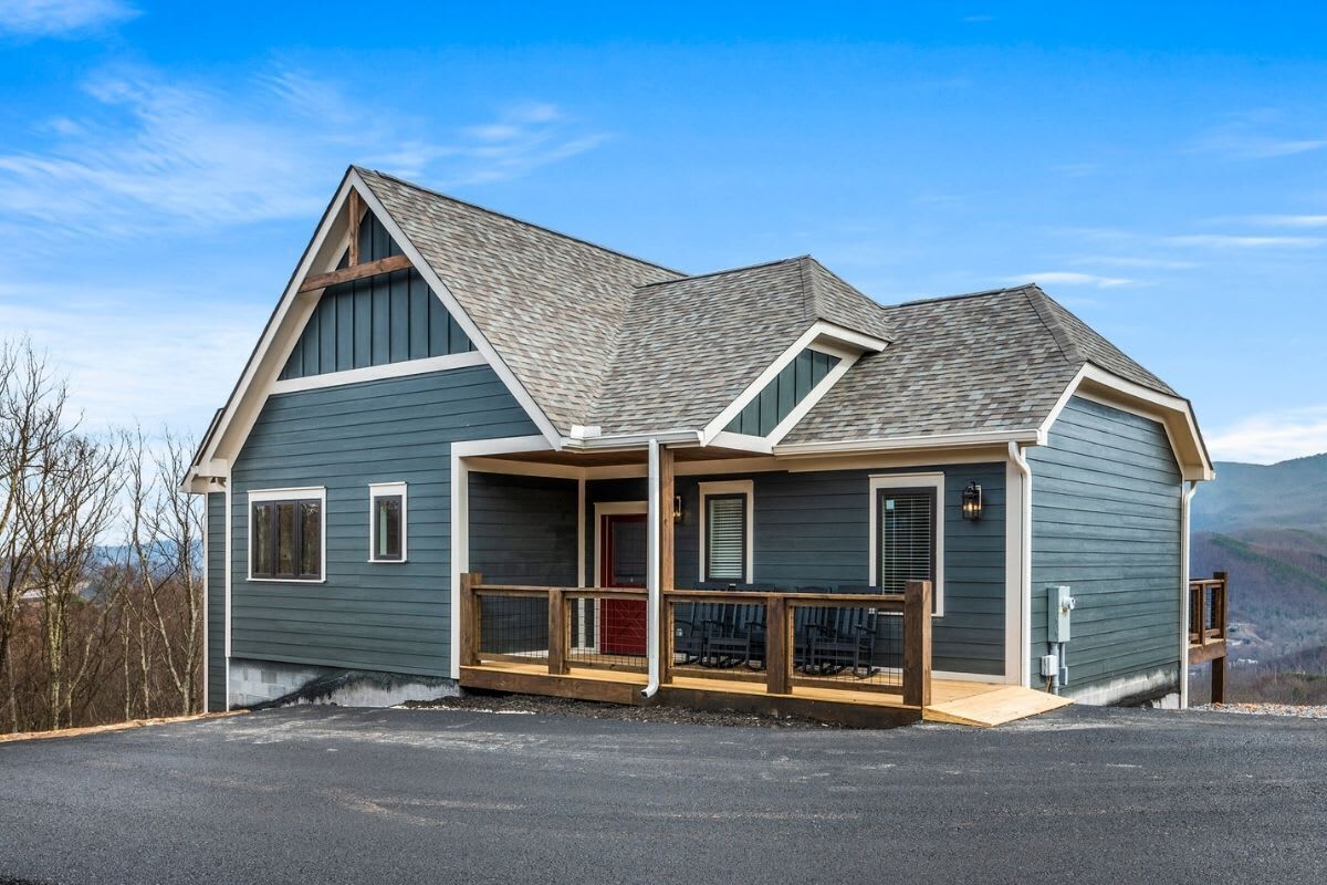 A two-story house with a porch, a red door, and a view of the mountains.