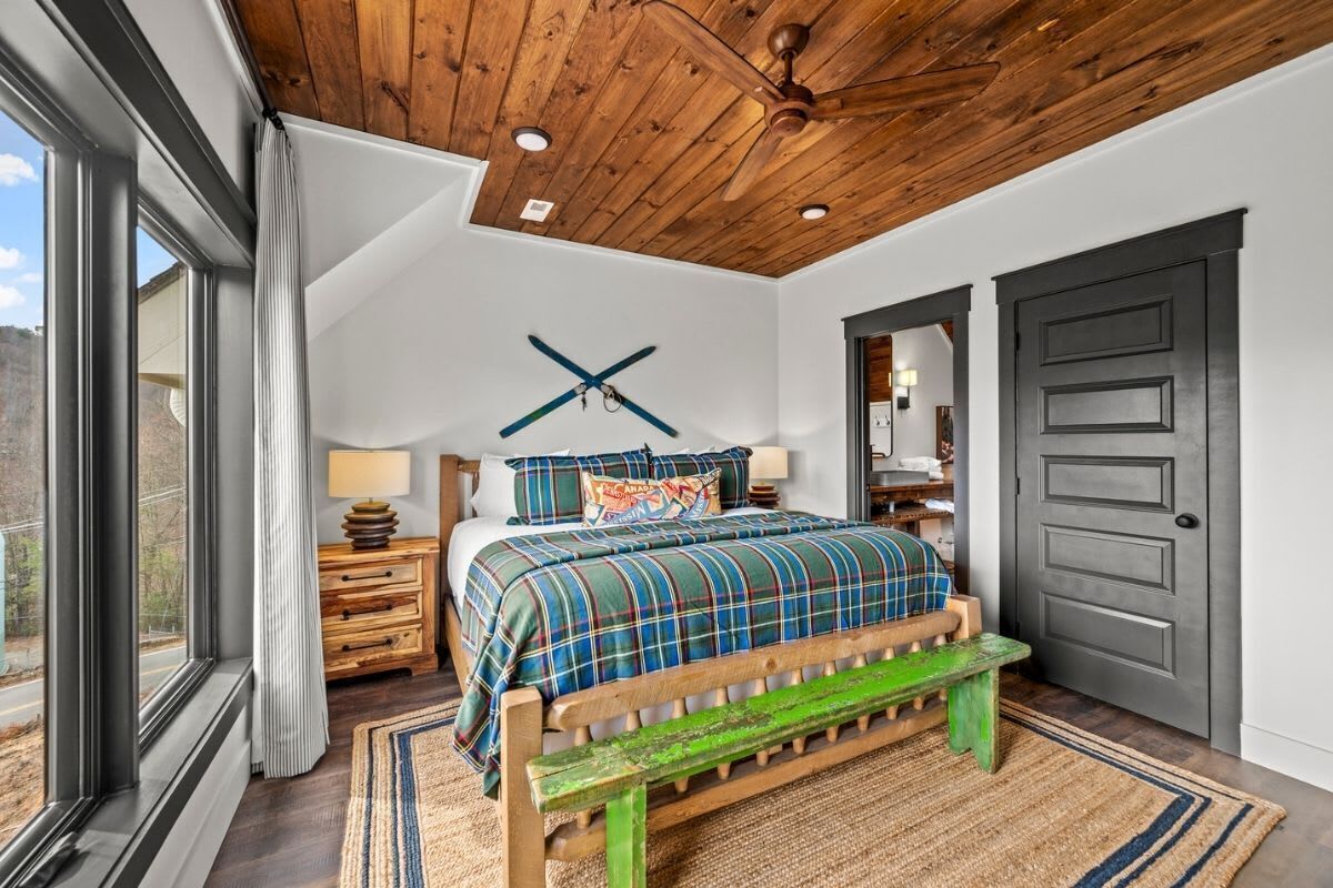 Een slaapkamer met een bed, een houten bankje en een plafondventilator.