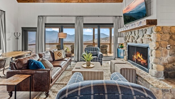 A spacious living room with a stone fireplace, leather sofas, and a large TV mounted on the wall.