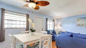 Ein Zimmer mit Esstisch, Stühlen, einem blauen Sofa, einem Deckenventilator und einem fenster mit Vorhängen.