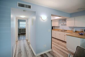 A modern kitchen with light blue walls, wooden flooring, and white cabinetry. - Idyllic Fort Pierce Retreat - Walk to Beach! (Fort Pierce)