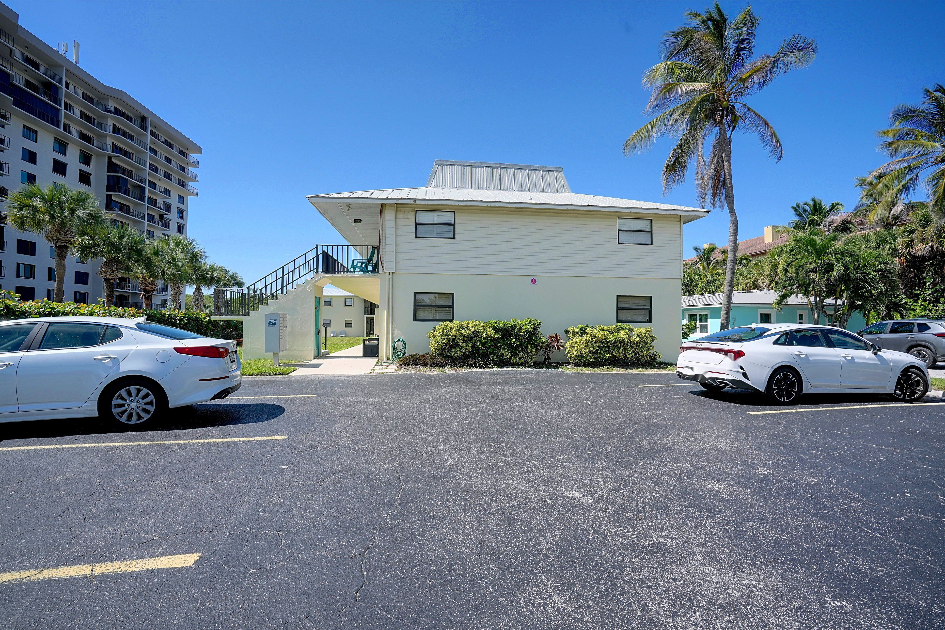 A two-story building with a flat roof, a front porch, and a parking lot with two white cars.