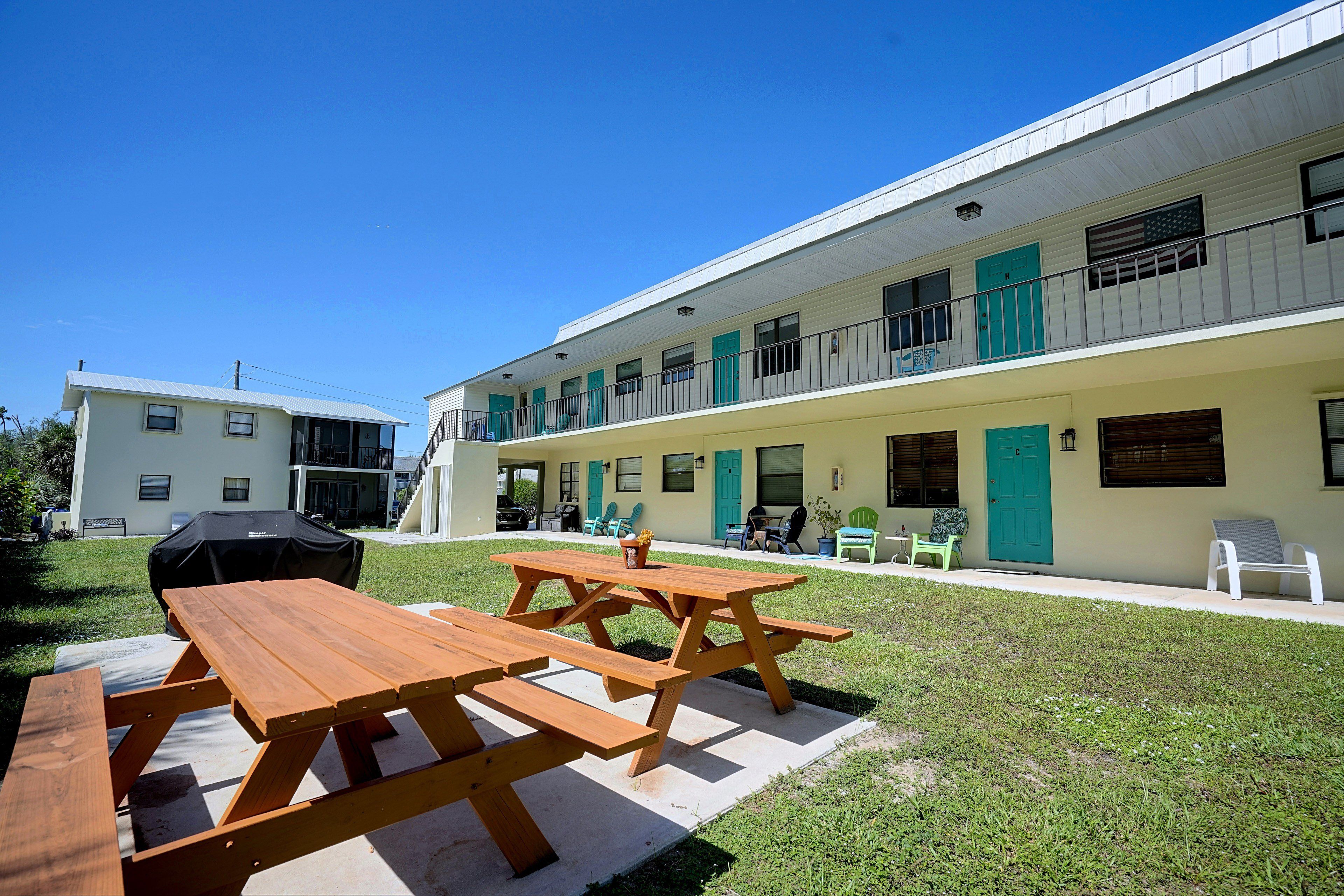 A building with a covered outdoor seating area, picnic tables, and a barbecue grill.