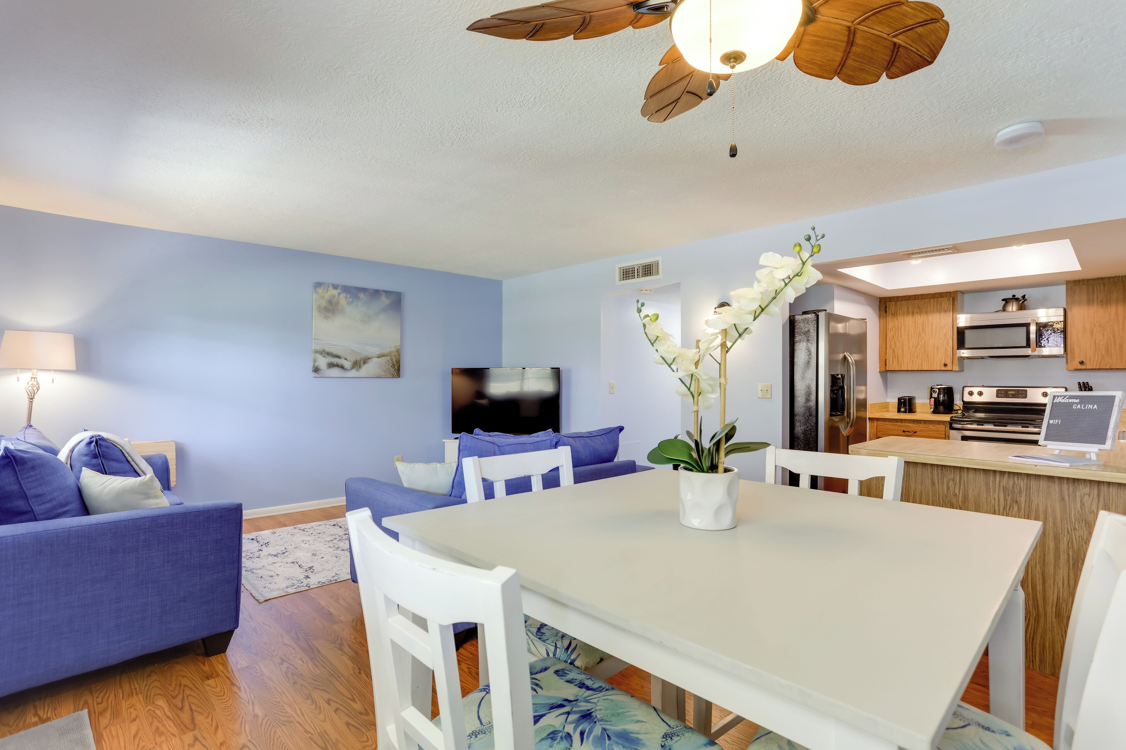 Una sala de estar moderna con un sofá azul, una mesa de comedor blanca y un ventilador de techo.