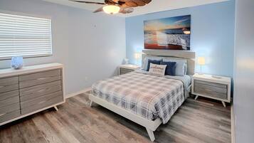 A bedroom with a bed, nightstands, a dresser, a ceiling fan, and a painting on the wall.