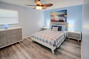 A bedroom with a bed, nightstands, a dresser, a ceiling fan, and a painting on the wall. - Idyllic Fort Pierce Retreat - Walk to Beach! (Fort Pierce)