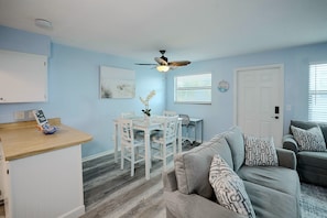 A living room with a grey sofa, a dining table with chairs, a ceiling fan, and a door with a window. - Idyllic Fort Pierce Retreat - Walk to Beach! (Fort Pierce)