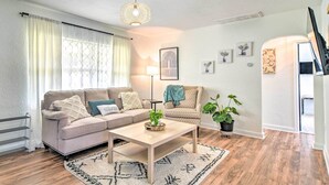 A modern living room with a beige sofa, a wooden coffee table, and a patterned rug. There is a potted plant and a framed picture on the wall. - Family-friendly Clearwater Home w/ Game Room! (Clearwater)
