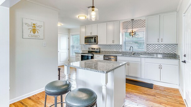 A modern kitchen with white cabinets, a granite countertop, and a central island with stools. - Pensacola Home w/ Covered Patio: 1 Mi to Downtown! (Pensacola)