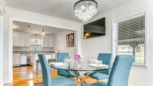 A dining area with a glass table, teal chairs, and a chandelier. - Pensacola Home w/ Covered Patio: 1 Mi to Downtown! (Pensacola)