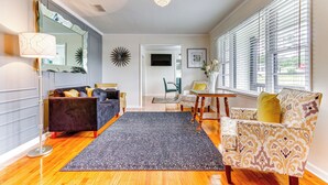 A living room with a dark patterned rug, a black sofa, a patterned armchair, a floor lamp, and a chandelier. - Pensacola Home w/ Covered Patio: 1 Mi to Downtown! (Pensacola)