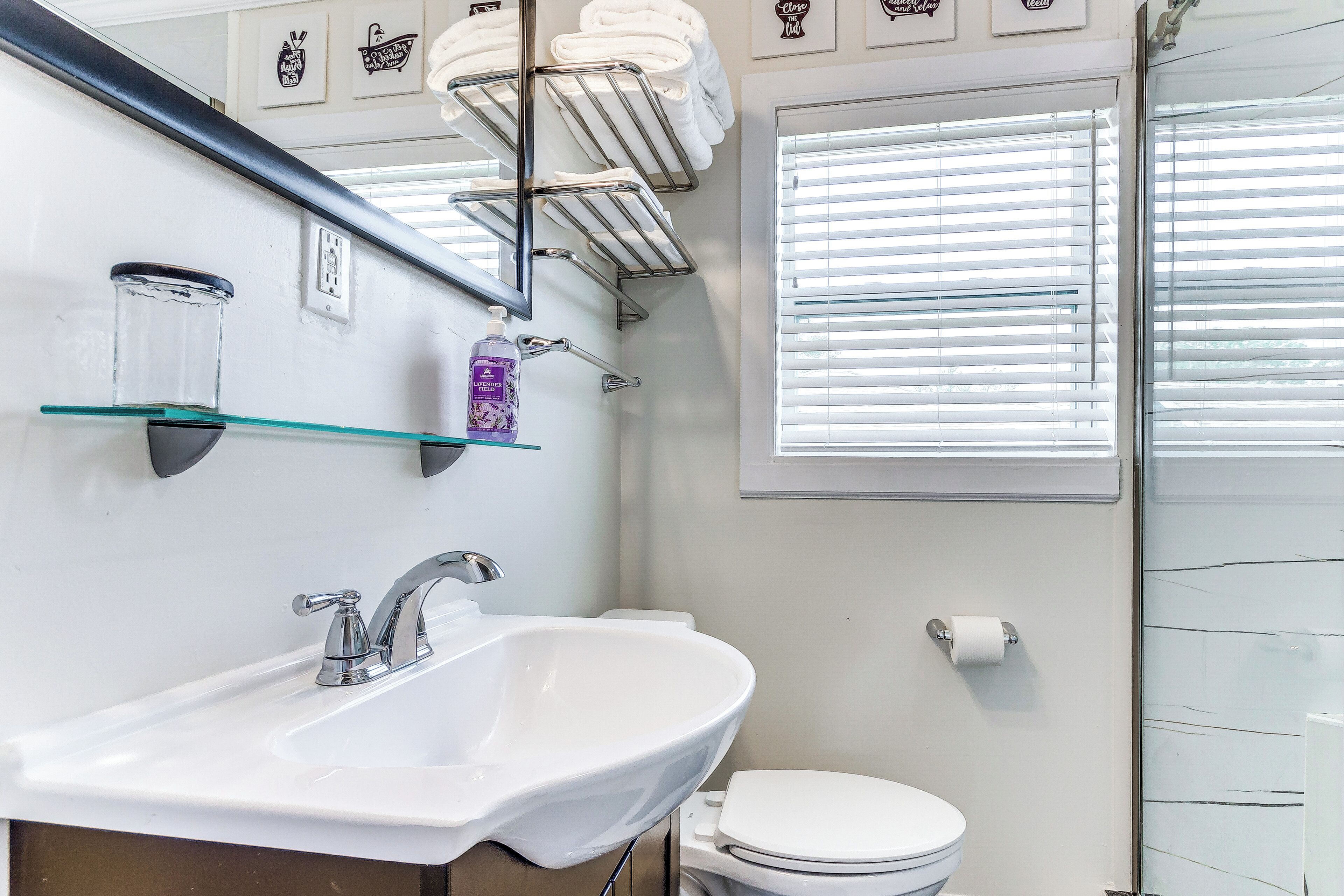 A bathroom with a white sink, a toilet, and a glass shelf holding towels.