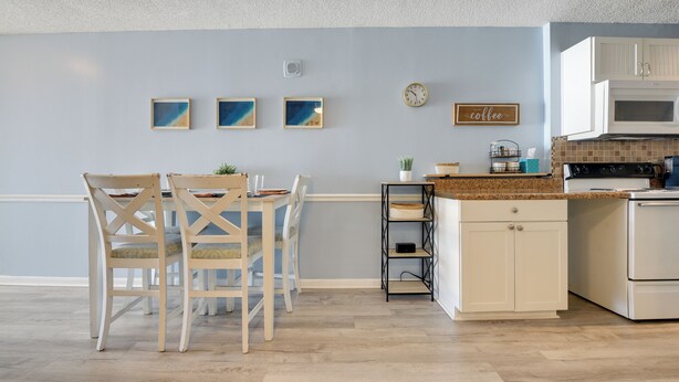 A kitchen with white cabinets, a microwave, and a clock on the wall. - Coastal Condo w/ Balcony in North Myrtle Beach! (North Myrtle Beach)