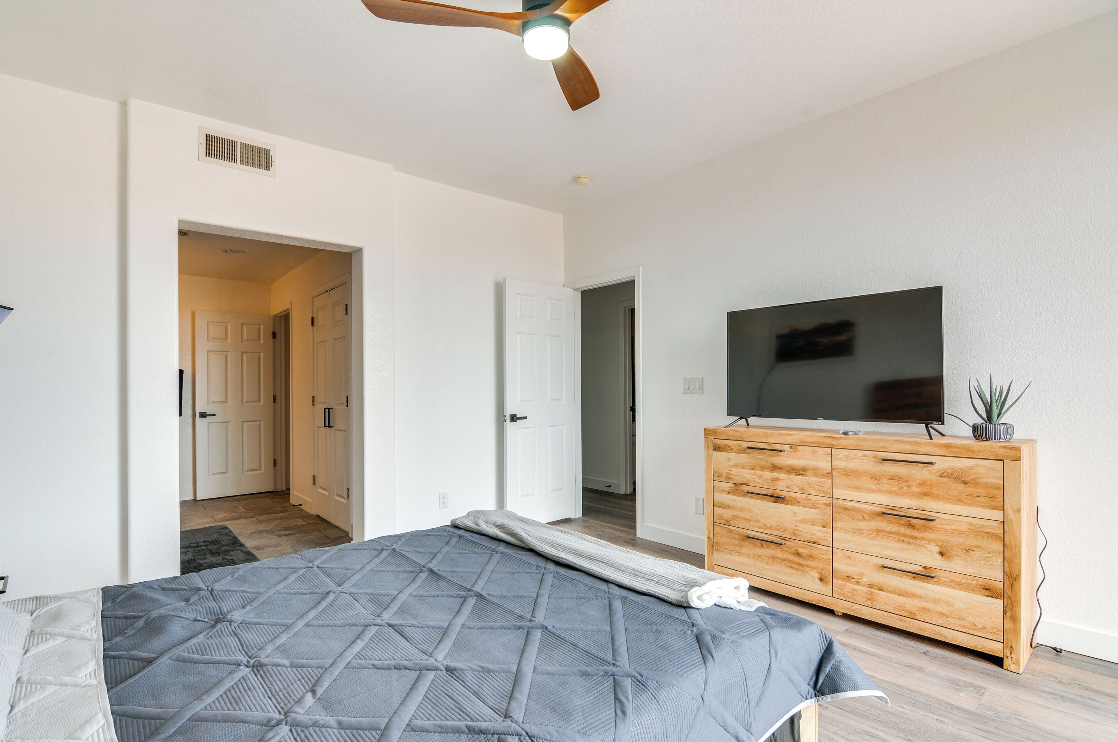 A bedroom with a bed, a wooden dresser, a television, and a ceiling fan.