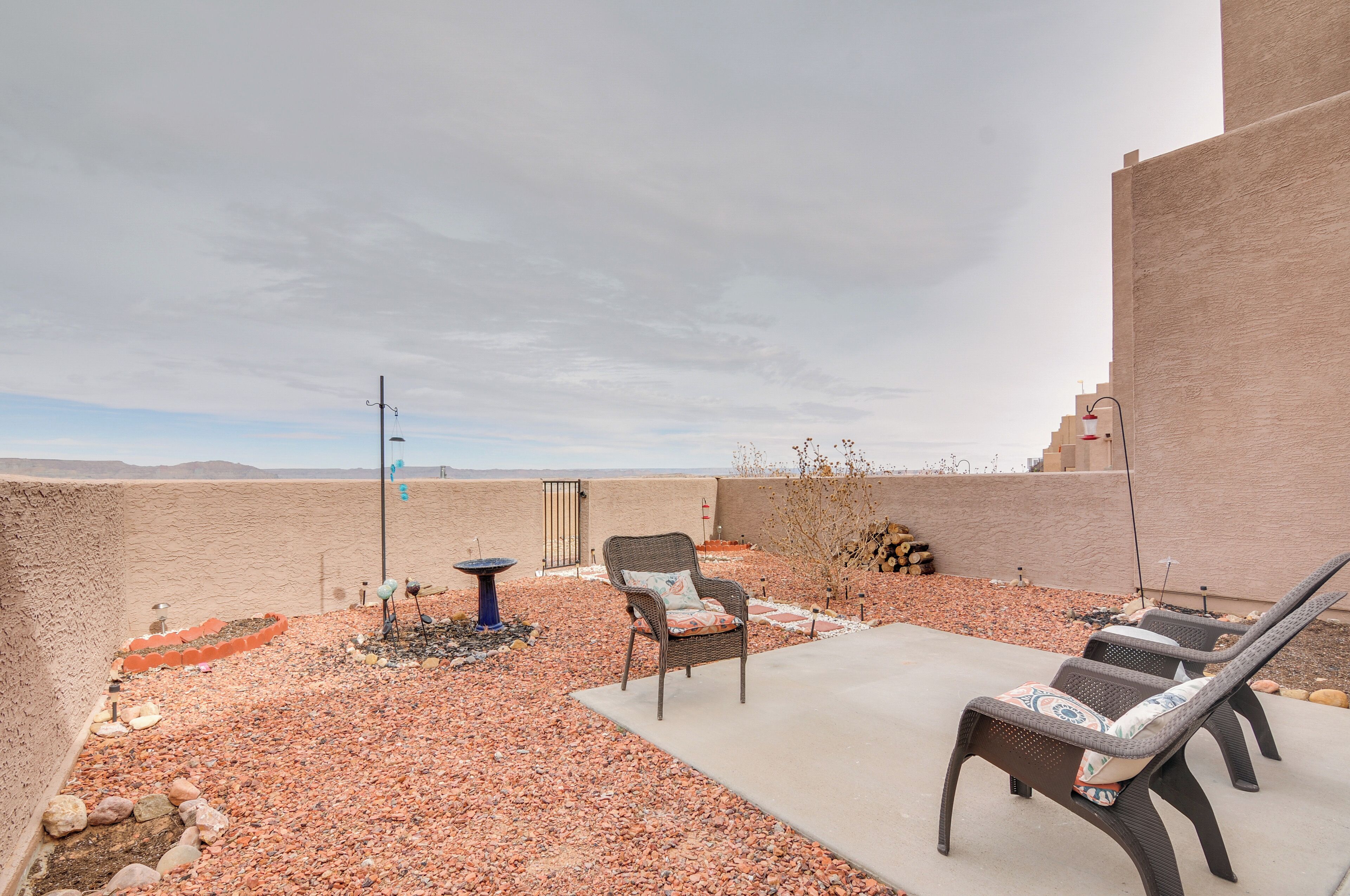 An outdoor patio with two wicker lounge chairs, a small table, and a decorative bird bath.