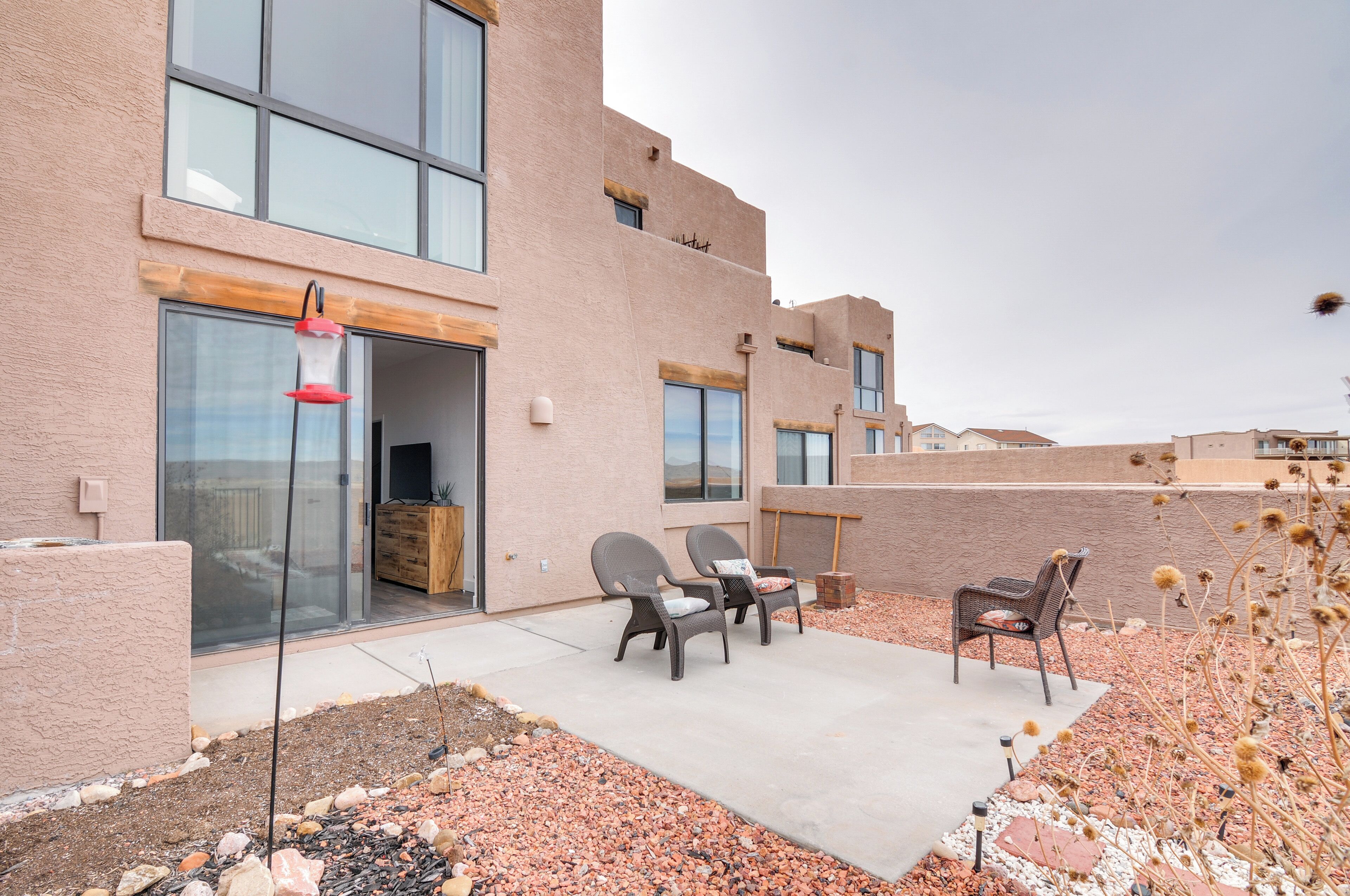 A modern building with a patio area featuring two chairs and a table, a red hanging light, and a gravel pathway.