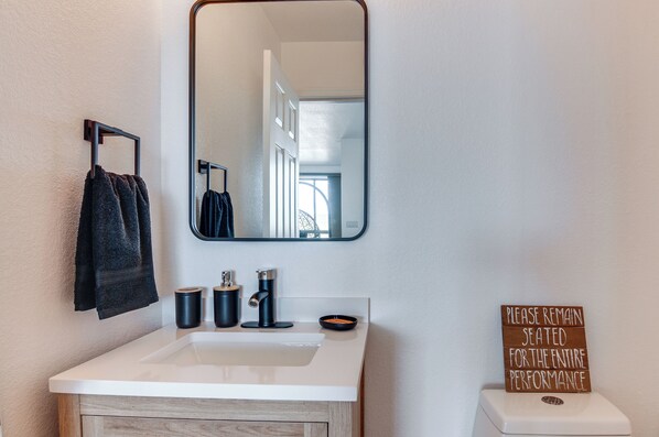 A bathroom with a white sink, black towel, and a sign on the wall. - Lake Powell Views: Adobe Townhome w/ Patio (Page)
