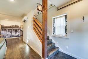 Una escalera de madera con escalones y un reloj, que conduce a una habitación con una ventana y un aire acondicionado instalado en la pared.