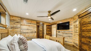 Ein Schlafzimmer einer Holzhütte mit Bett, Kissen, Deckenventilator und Fernseher.