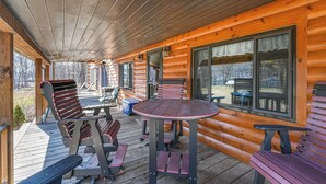 A covered deck with wooden furniture, including chairs and a table, and large windows along the walls. - Cozy Mount Union Cabin w/ Fire Pit & River Access (Mount Union)