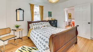 A bedroom with a wooden bed, a small table with a plant, a chair, and a view of another room through an open door. - Danville Rental, Walk to Caesars Virginia Casino (Danville)